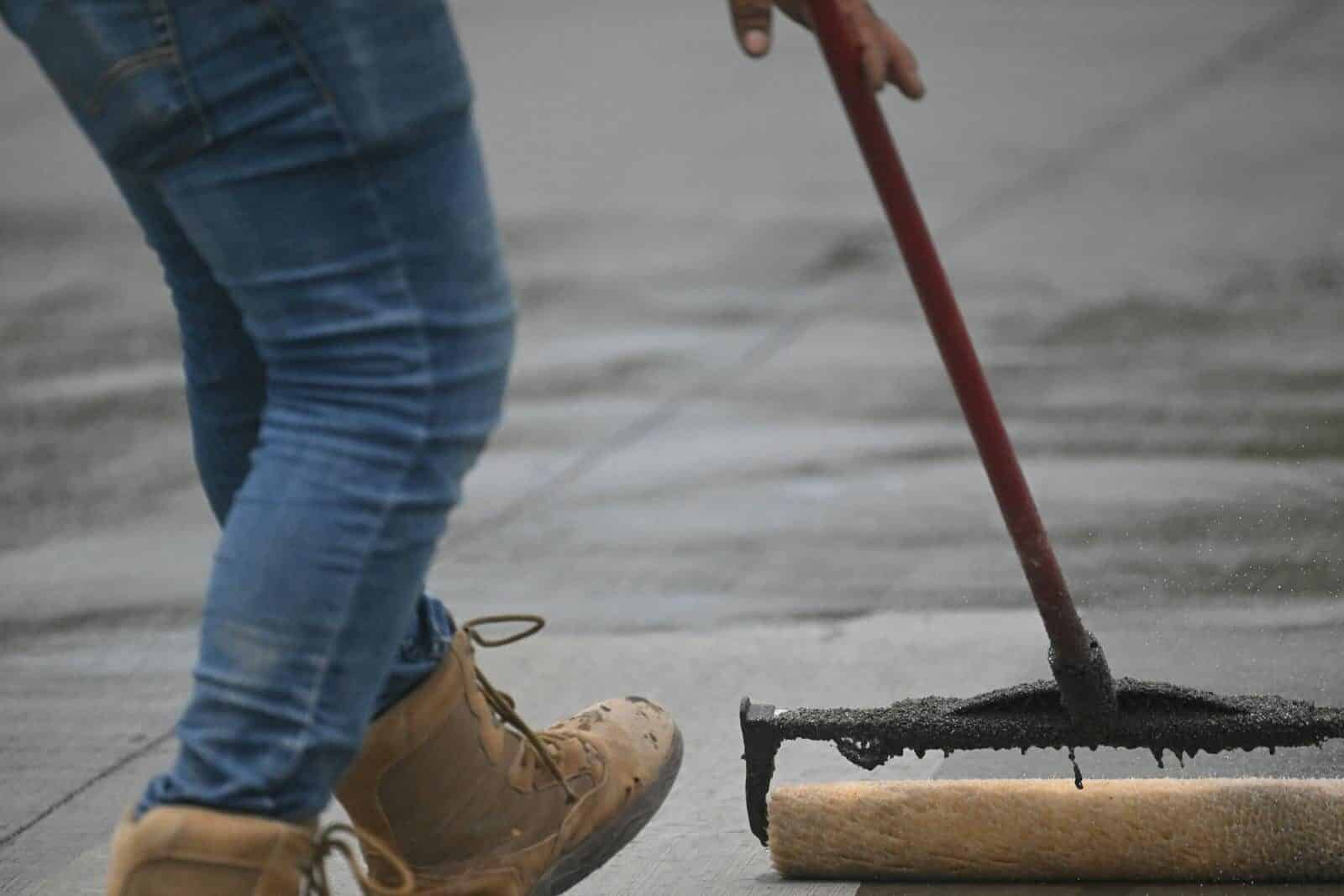 Detailed image of concrete sealing with a roller on pavement, showing boots and jeans in action.